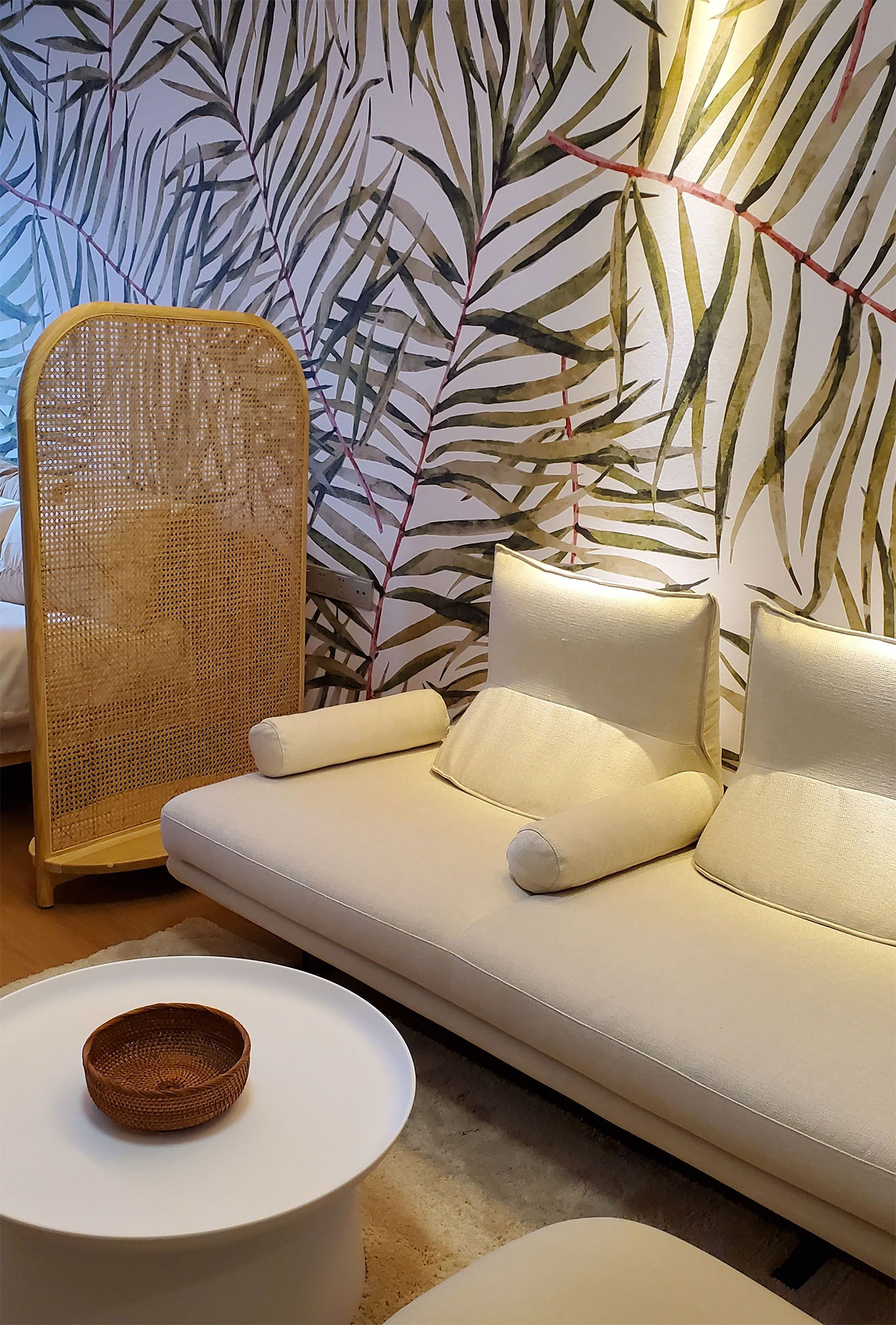 jasna sofa i rattanowe dodatki przy roślinnej ścianie