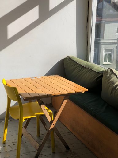 mały słoneczny balkon ze stolikiem, ławką i żółtym krzesłem