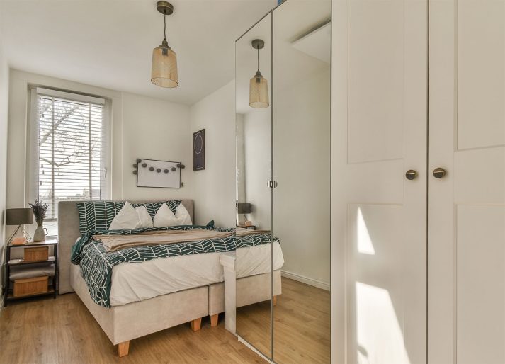 mała sypialnia z szafą z lustrem i łóżkiem przy ścianie