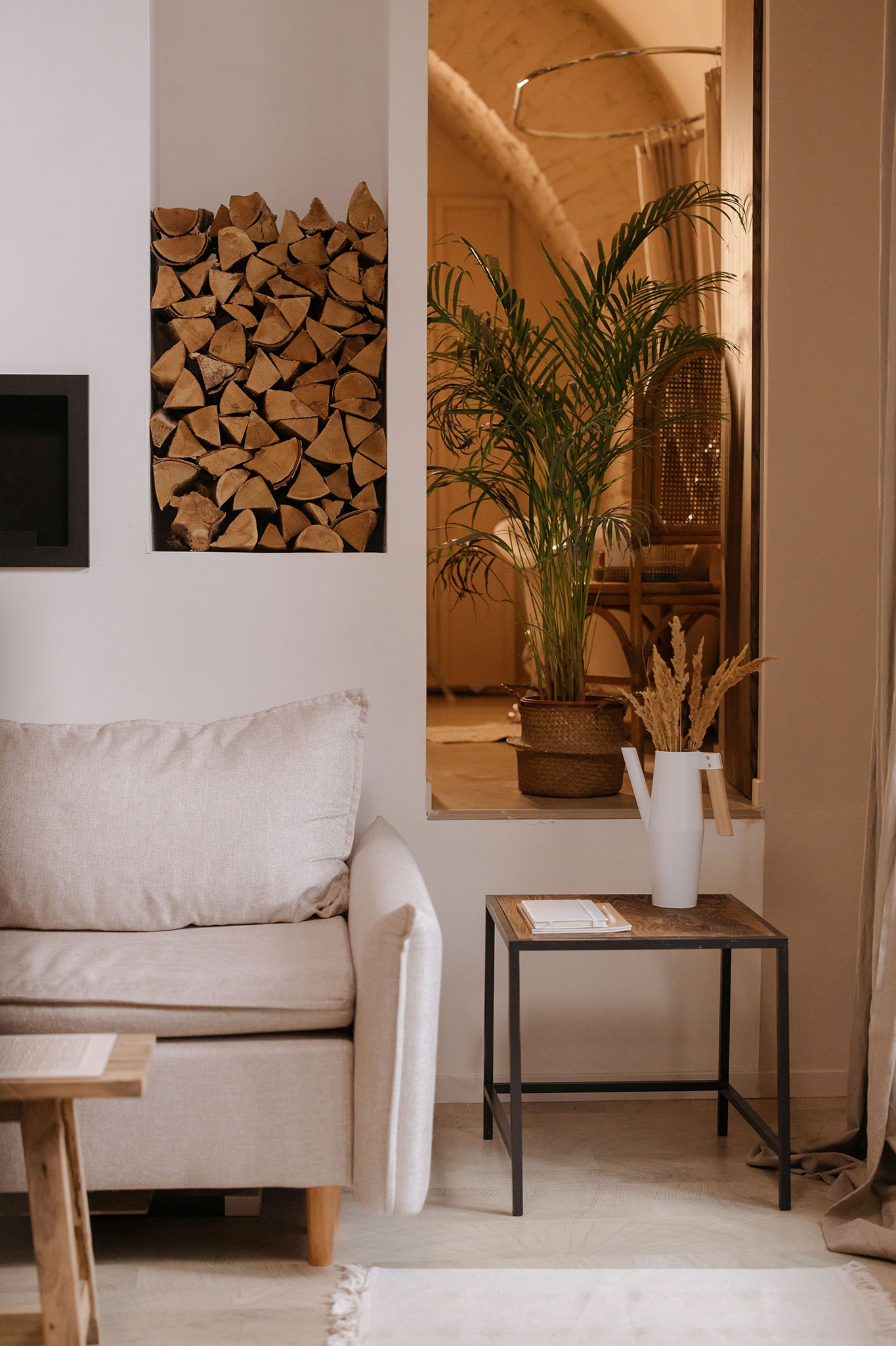 Jasny salon boho z beżową sofą, rośliną i drewnianymi dodatkami