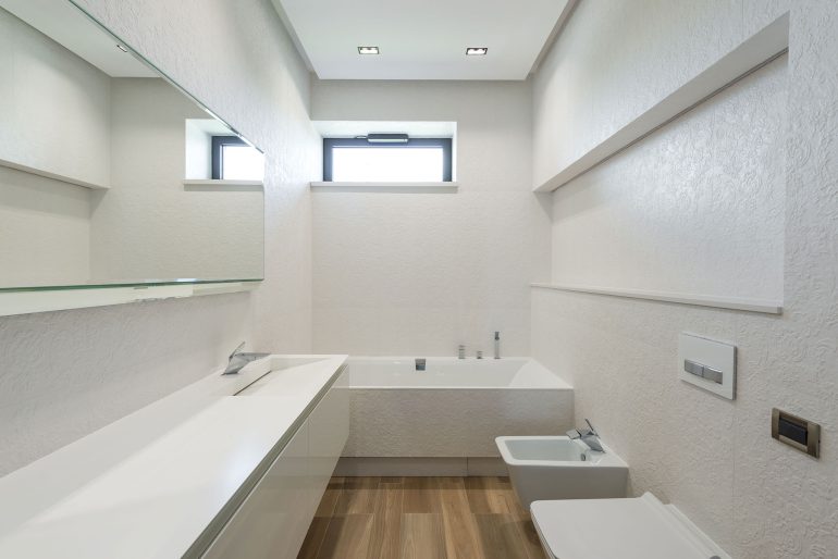 Wąska łazienka z oknem na końcu, wanną, umywalką i WC